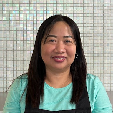 Dolores, exuding warmth and expertise, stands in her professional attire, symbolizing her dedication to waxing, sugaring, and threading services at Aroma Waxing Clinic