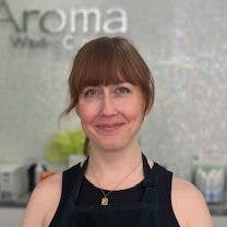 Laura Hopkins, beaming with enthusiasm, stands in her professional attire, symbolizing her blend of joy and expertise in waxology and medical esthetics at Aroma Waxing & Laser Clinic